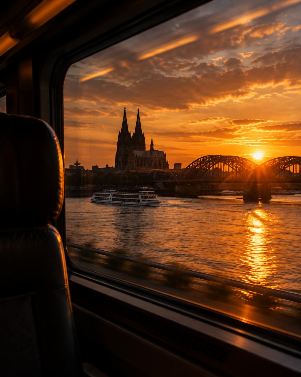 A train window at sunset overlooking a river, a bridge and a cathedral skyline